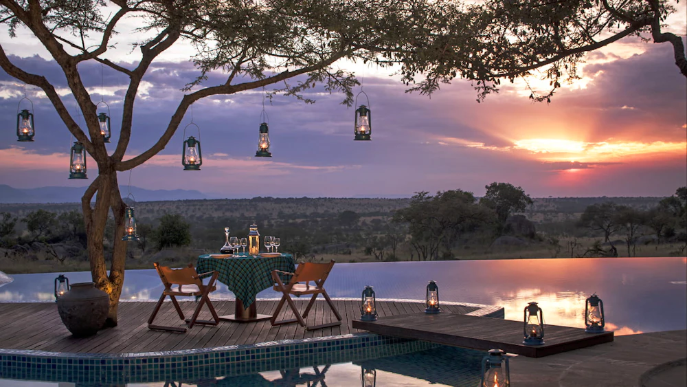 A lantern-lit pool deck overlooking the Serengeti plains at sunset, Tanzania
