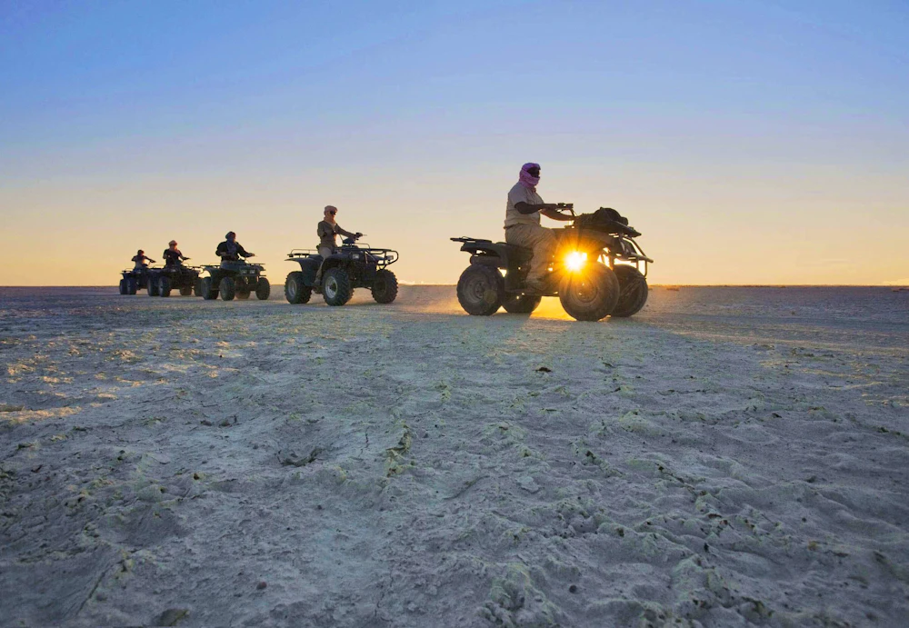 A line of quad bikes crossing the white Makgadikgadi salt pans at sunset, Botswana