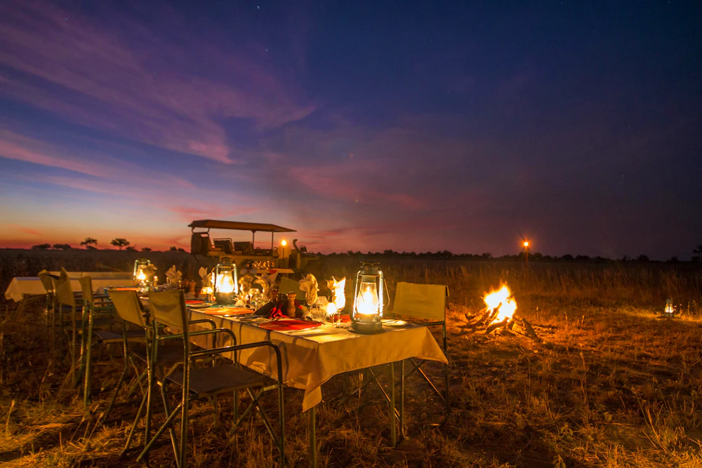 A lantern-lit bush dinner with a campfire at dusk in the Kwando Reserve, Botswana
