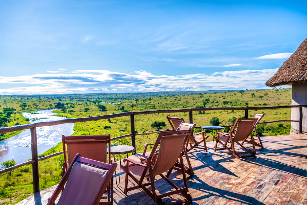 Safari chairs on a camp deck overlooking a river and the Serengeti plains, Tanzania
