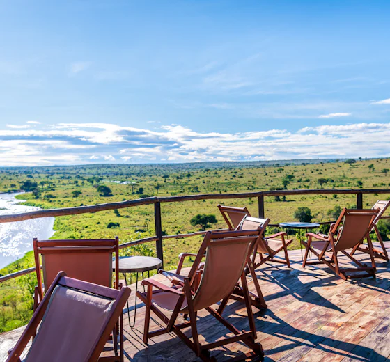 Safari chairs on a camp deck overlooking a river and the Serengeti plains, Tanzania