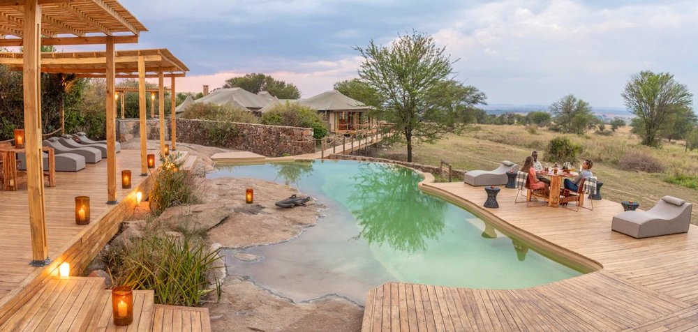 A pool and lounge deck at golden hour with tents behind at Sayari Camp, Serengeti, Tanzania