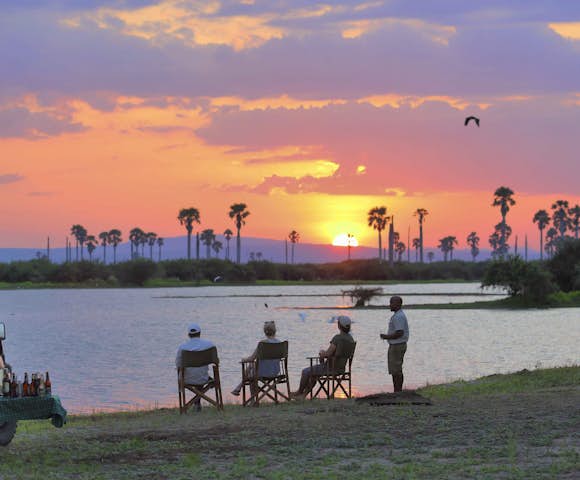 People sitting in front of lake with sunset, Selous Game Reserve